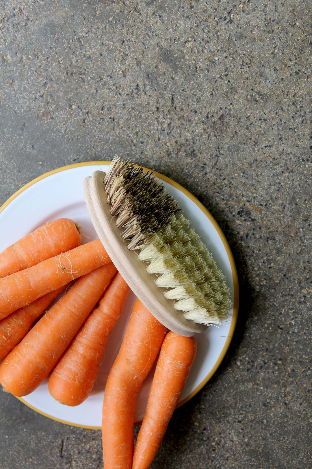 Carrots on a plate with a scrubbing brush on a concrete surface
