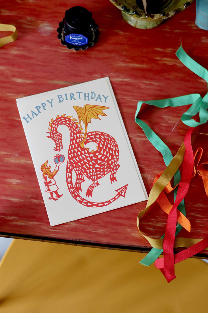 Birthday card with dragon design on a red surface with ribbons