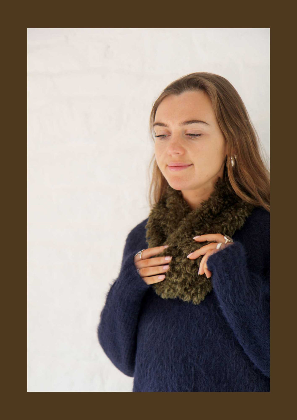 Woman wearing a dark blue sweater and green scarf against a white background