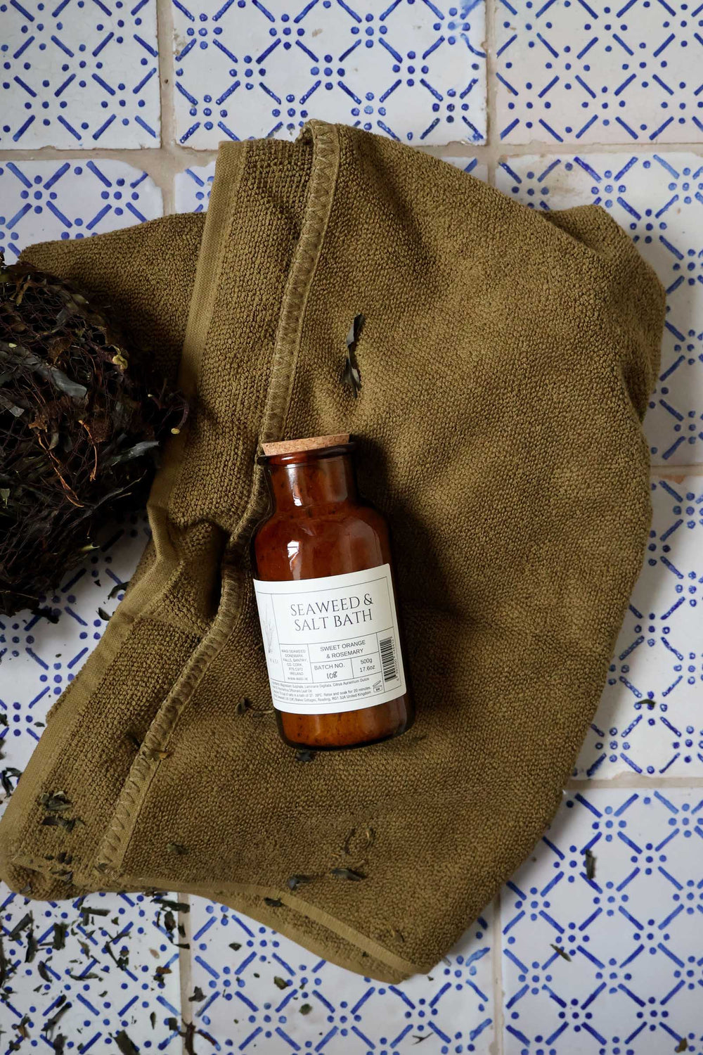 Bottle of 'Herbal & Salve Bath' on a brown cloth against a tiled wall background