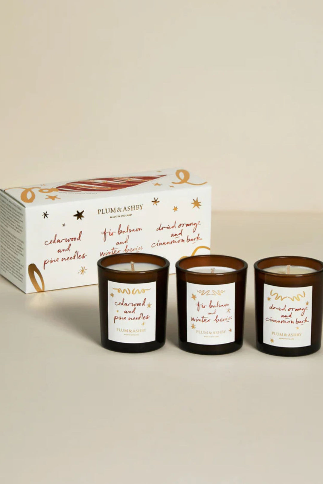 Three candles with labels and a box in the background on a beige surface