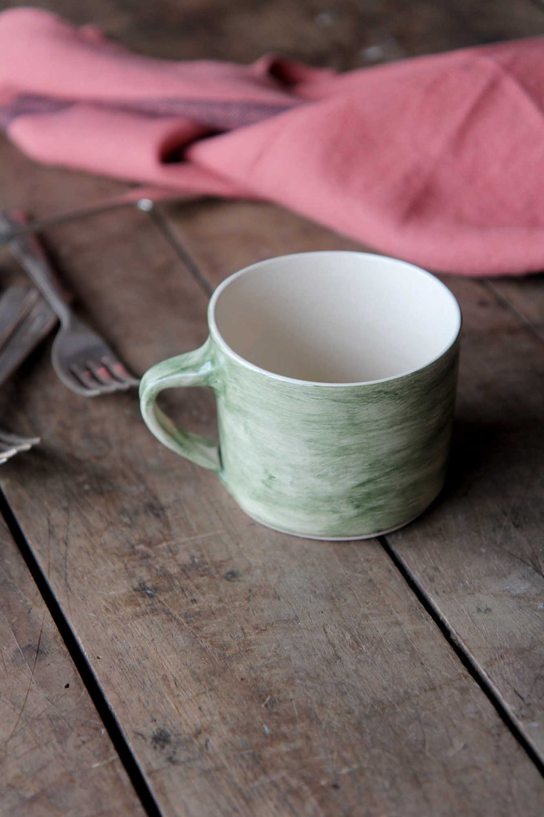 Green ceramic mug on a wooden surface with a pink cloth in the background