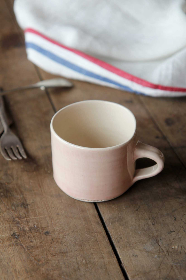 Pink ceramic mug on a wooden surface with a striped fabric in the background
