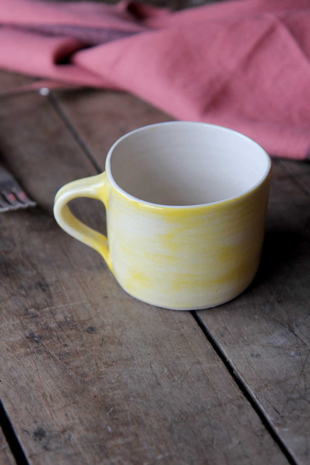 Yellow mug on a wooden surface with a pink cloth in the background