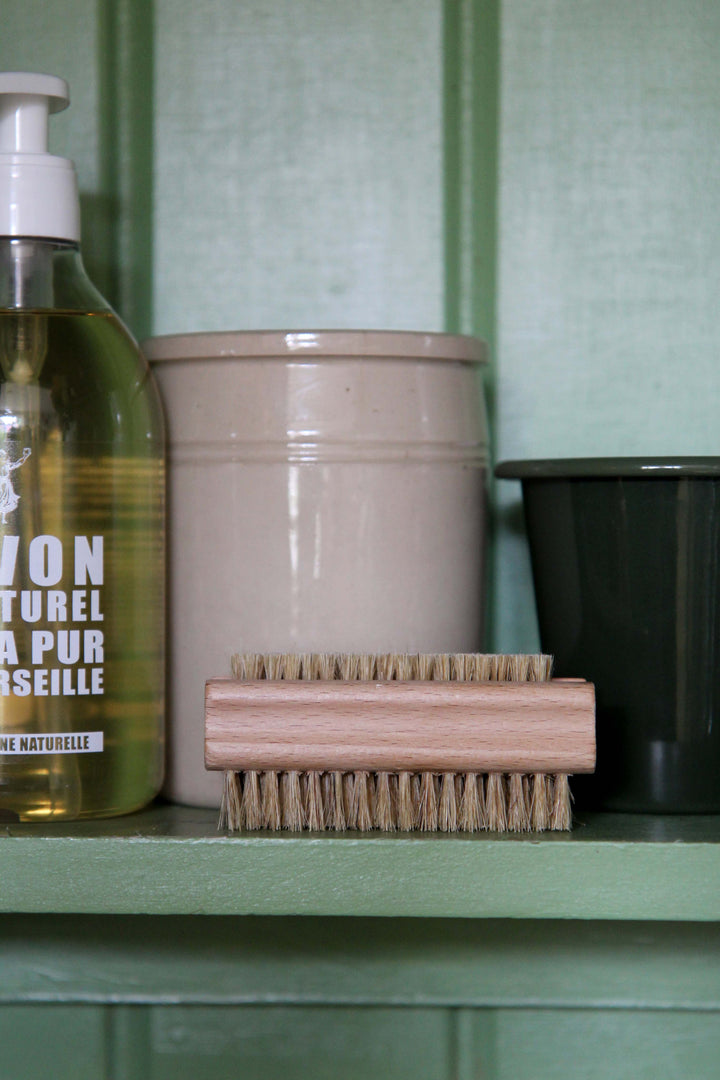 Bottle of natural soap, beige container, and wooden brush on a green shelf.
