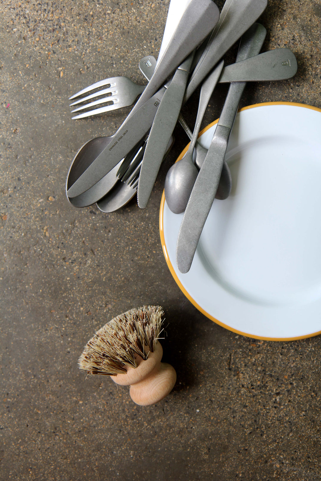 Silverware on a plate with a dish brush on a concrete surface