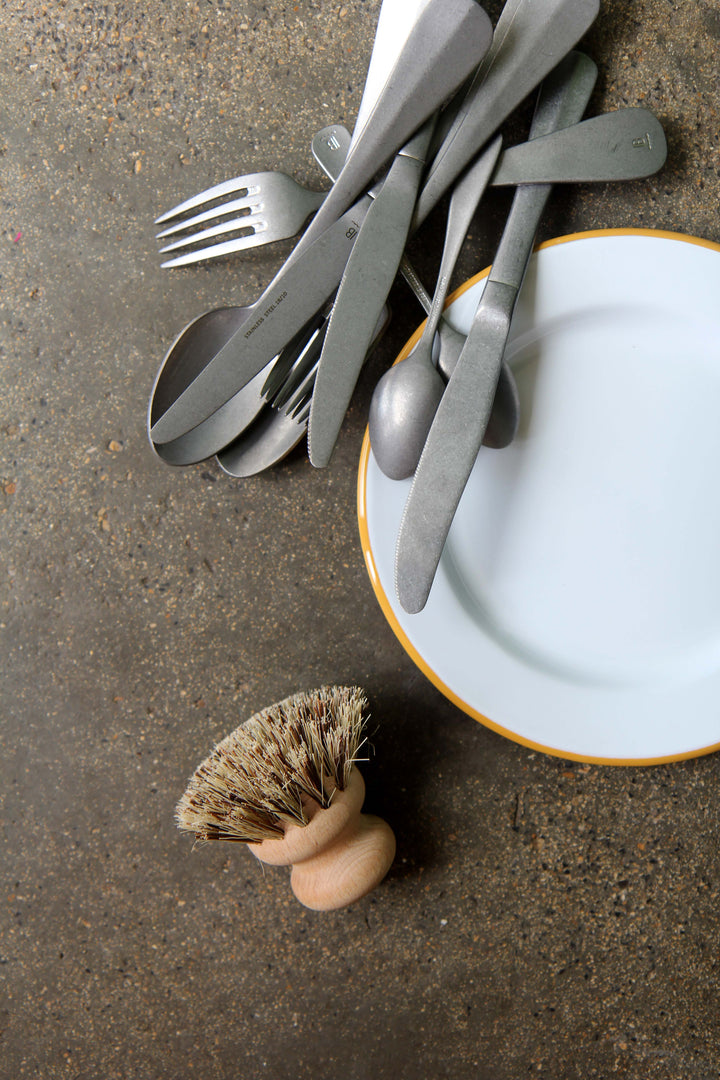 Silverware on a plate with a dish brush on a concrete surface