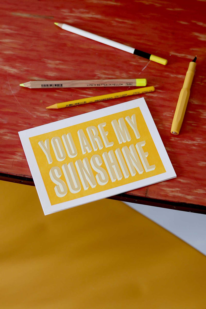 Card with 'You are my sunshine' text on a wooden surface with pencils.