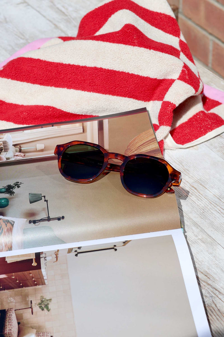 Round sunglasses on a magazine with a red and white striped towel in the background