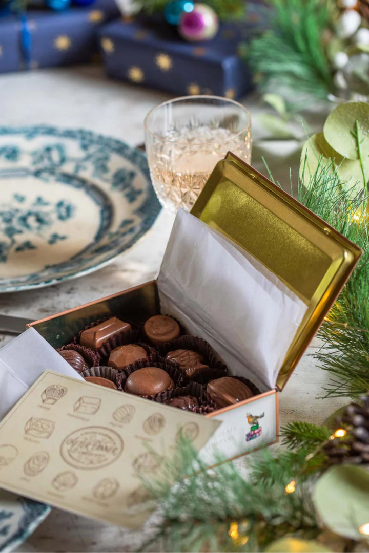 Box of chocolates with a gold lid on a festive table setting with Christmas decorations.