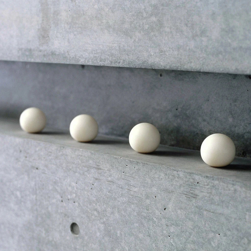 Four white spherical soaps on a concrete surface with a concrete wall in the background.