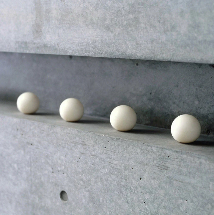 Four white spherical soaps on a concrete surface with a concrete wall in the background.