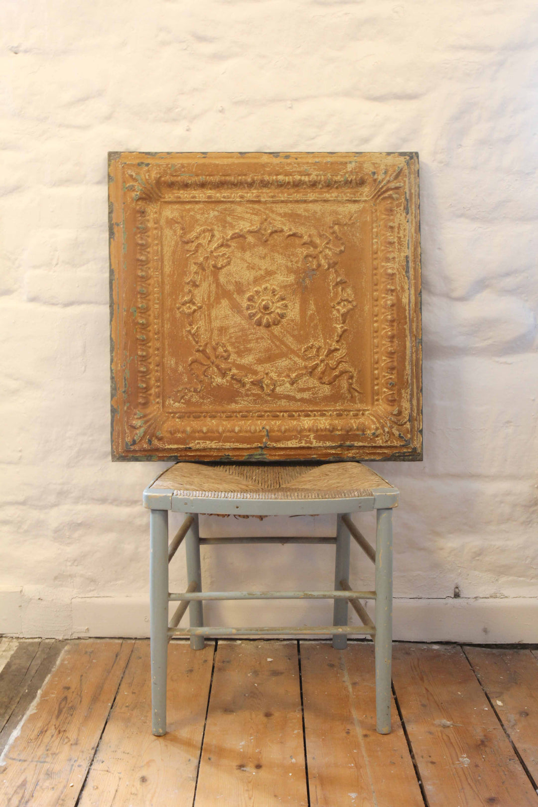 Decorative wooden panel with intricate design on a stool against a textured white wall.