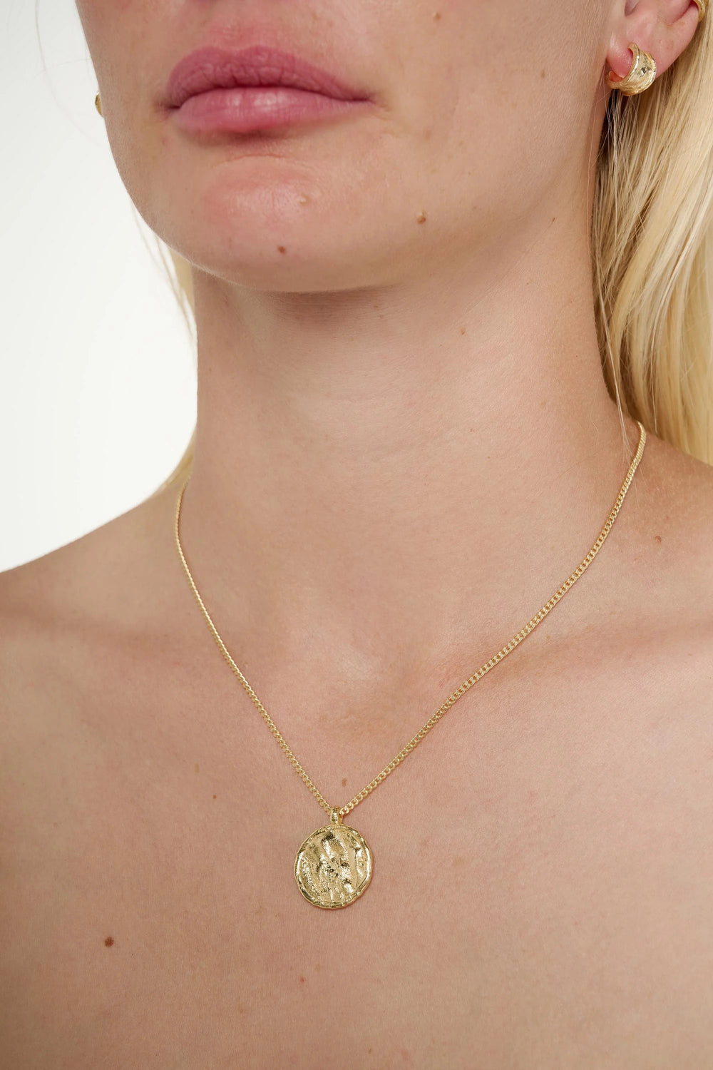 Close-up of a person wearing a gold necklace with a pendant on a plain background