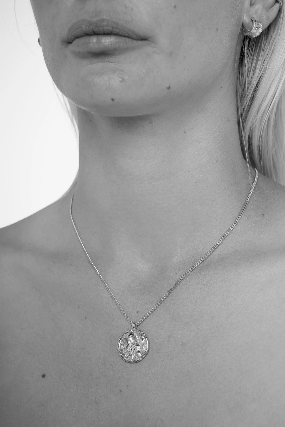 Close-up of a person wearing a necklace with a pendant on a plain background