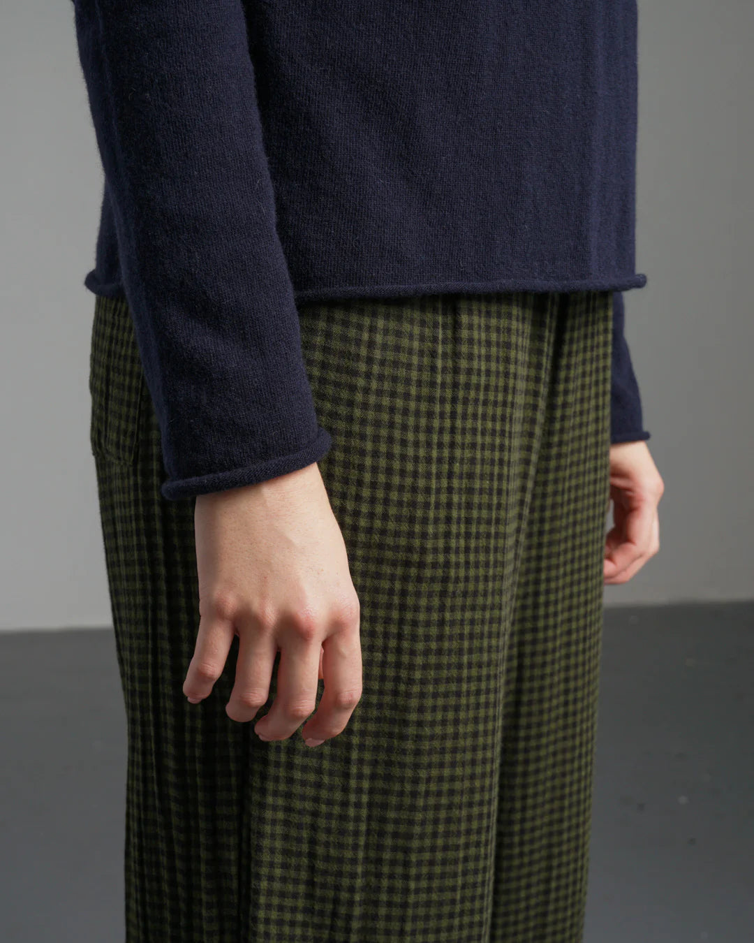 Person wearing a navy sweater and green checkered pants against a gray background