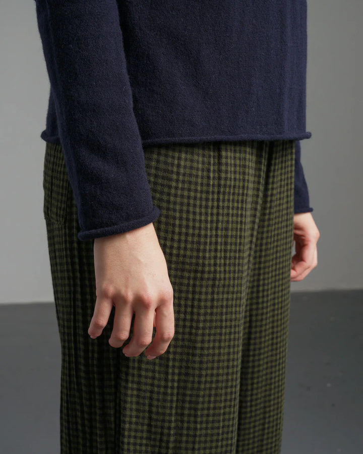 Person wearing a navy sweater and green checkered pants against a gray background
