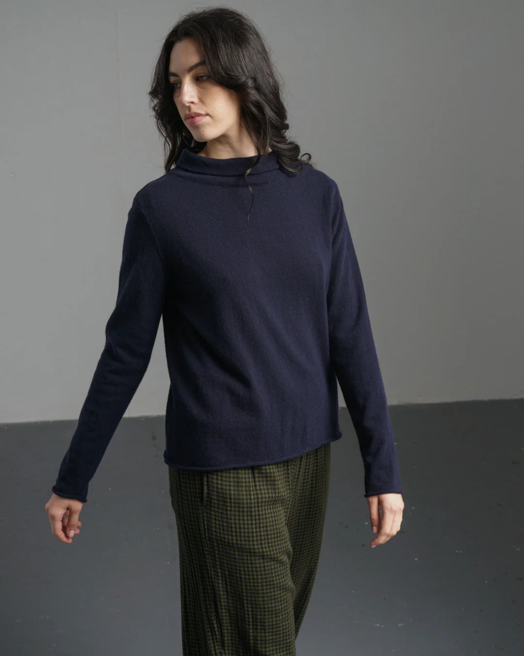 Woman wearing a navy blue sweater and green plaid pants against a gray background