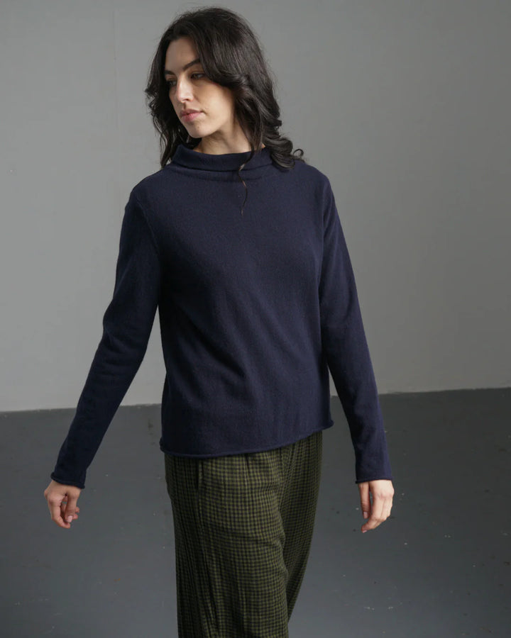 Woman wearing a navy blue sweater and green plaid pants against a gray background