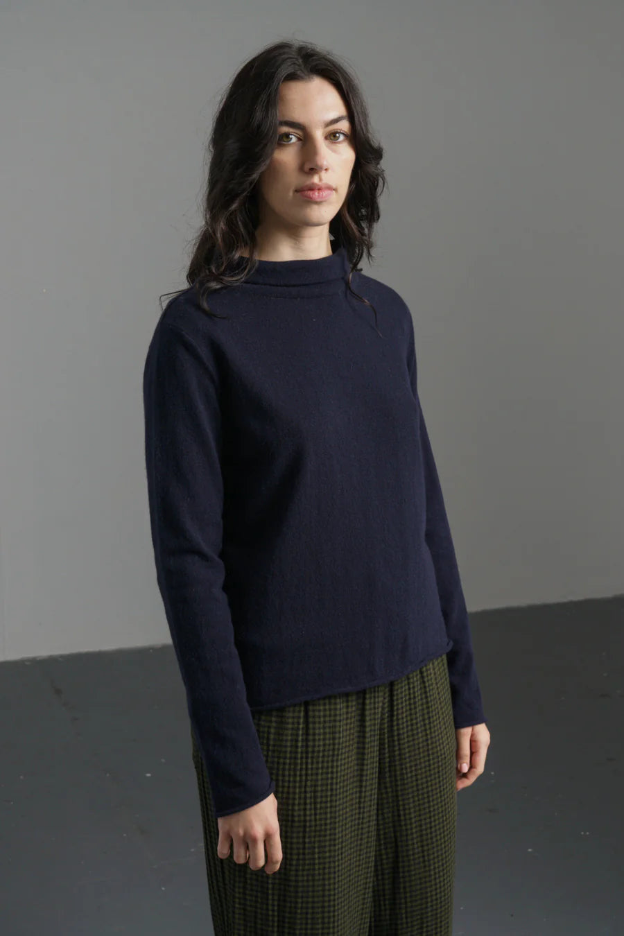 Woman wearing a navy sweater and green plaid pants against a gray background