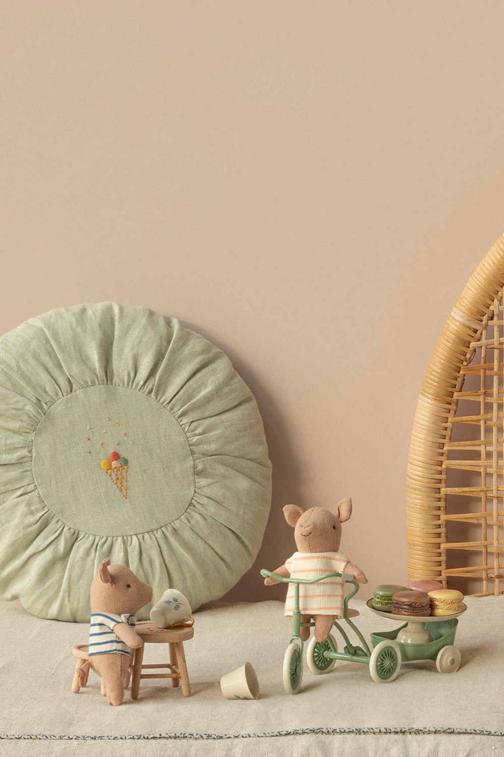 Two small pigs with a green cushion and wicker basket on a light surface.