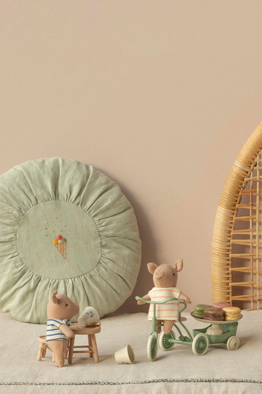 Two small pigs with a green cushion and wicker basket on a light surface.