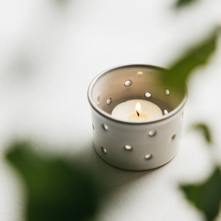 White ceramic candle holder with a lit t-light candle on a light background