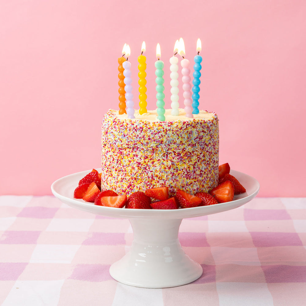 Birthday cake with colourful candles and sprinkles on a pink background