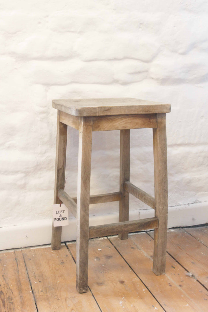 Wooden stool against a textured white wall on a wooden floor