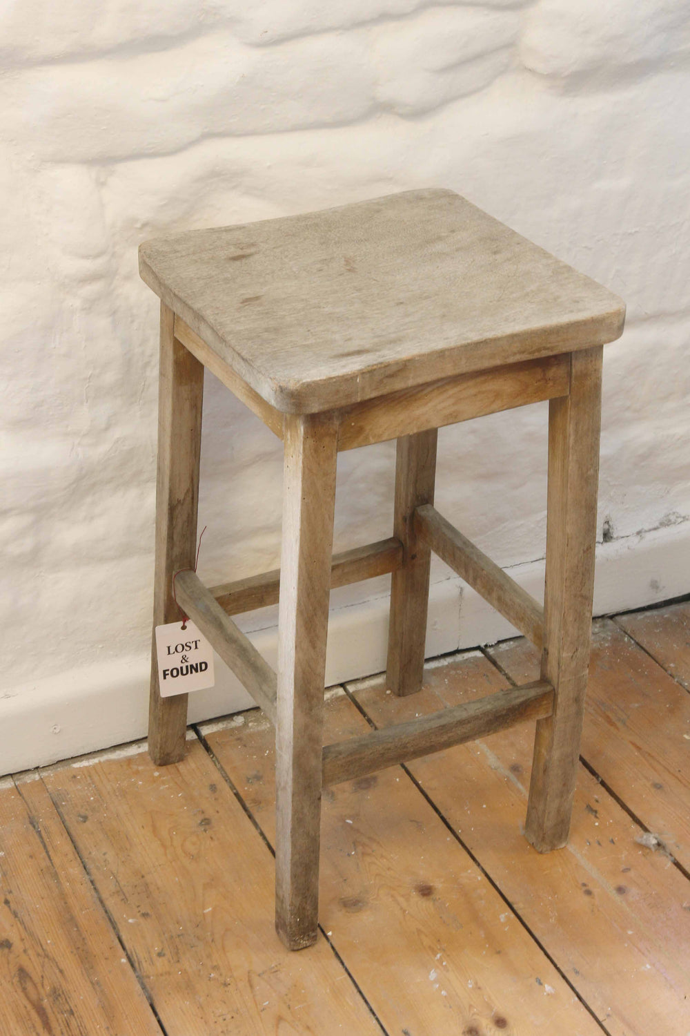 Wooden stool with a stone top on a wooden floor against a textured white wall.