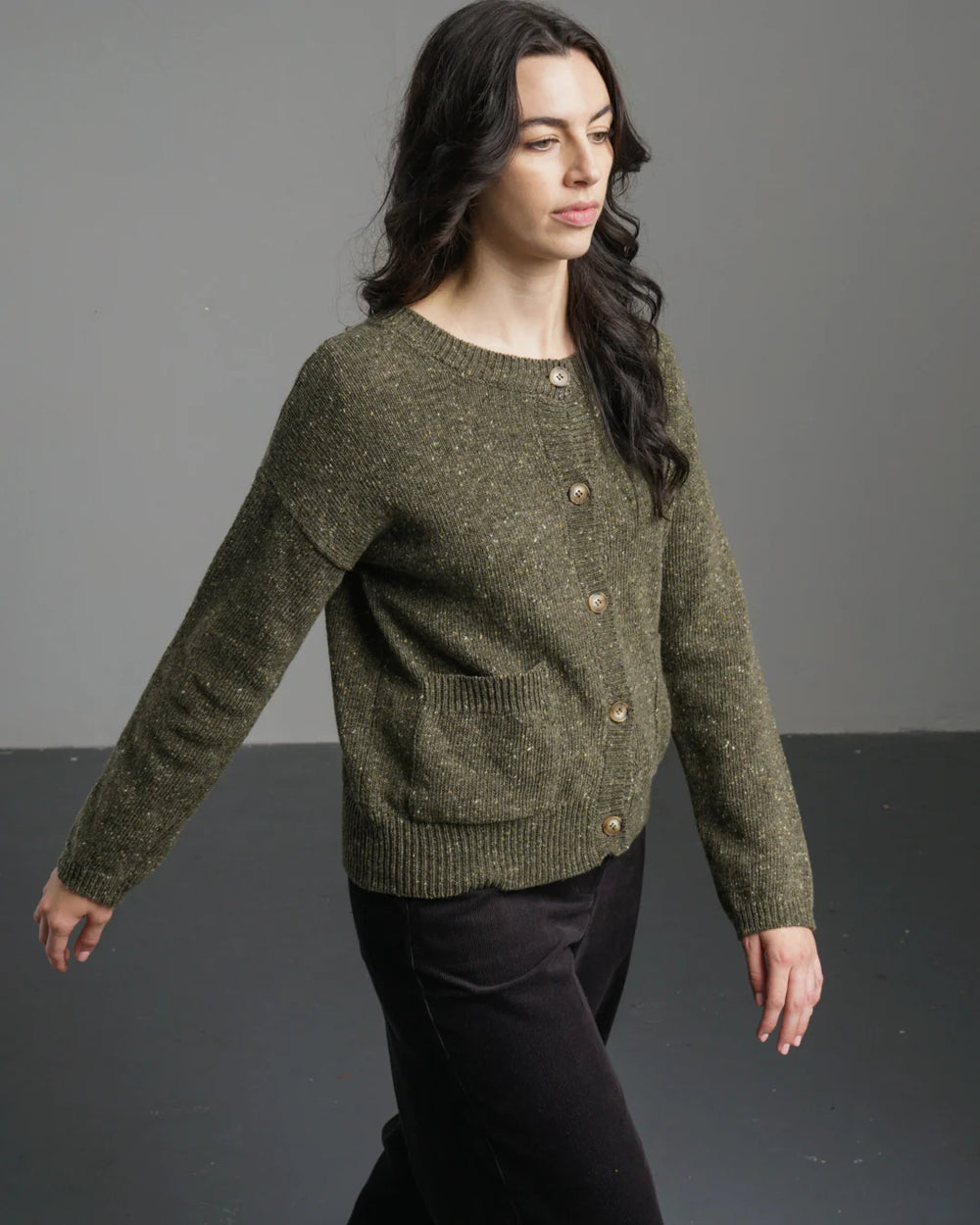 Woman wearing a green knitted sweater with buttons against a gray background