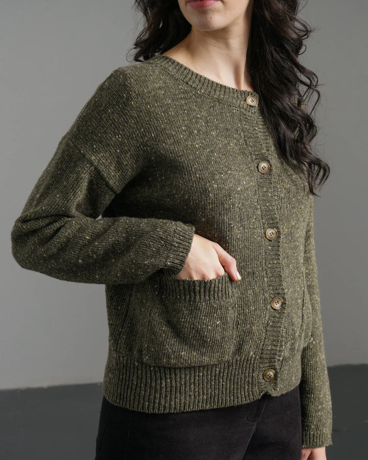 Person wearing a green knitted cardigan with buttons against a gray background