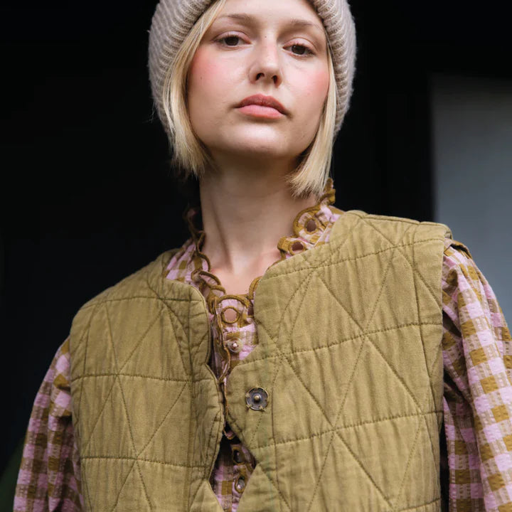 Person wearing a quilted vest over a plaid shirt with a neutral background