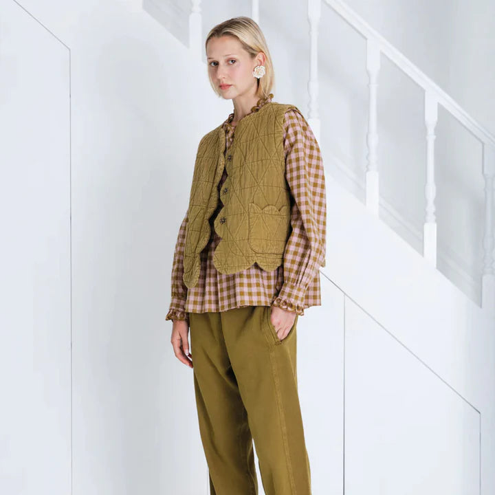 Woman wearing a green knitted vest over a plaid shirt with matching pants against a white background