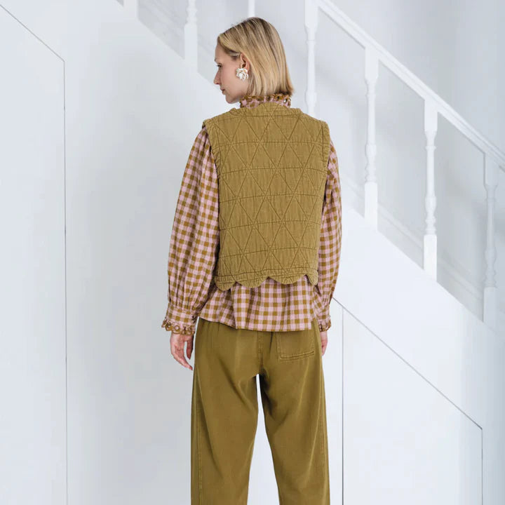 Person wearing a green checkered vest over a plaid shirt with matching pants in a minimal white setting