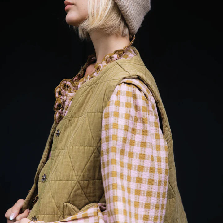 Person wearing a green quilted vest over a plaid shirt with a black background