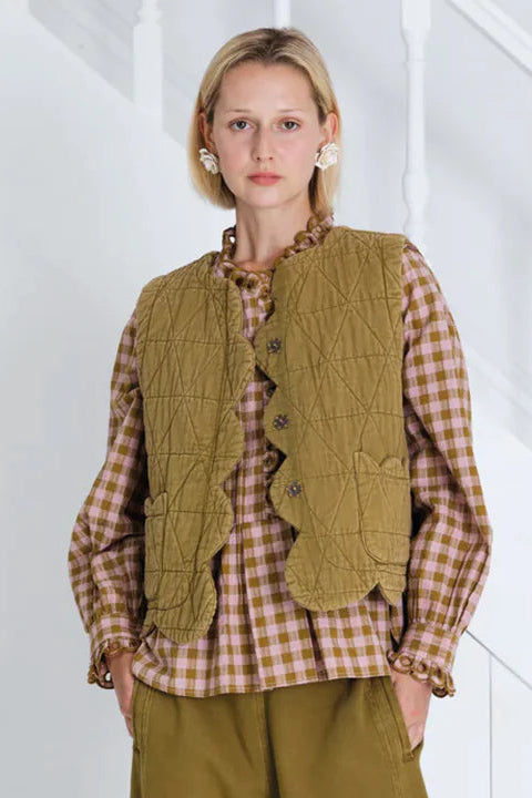 Woman wearing a green vest over a plaid shirt with a white background