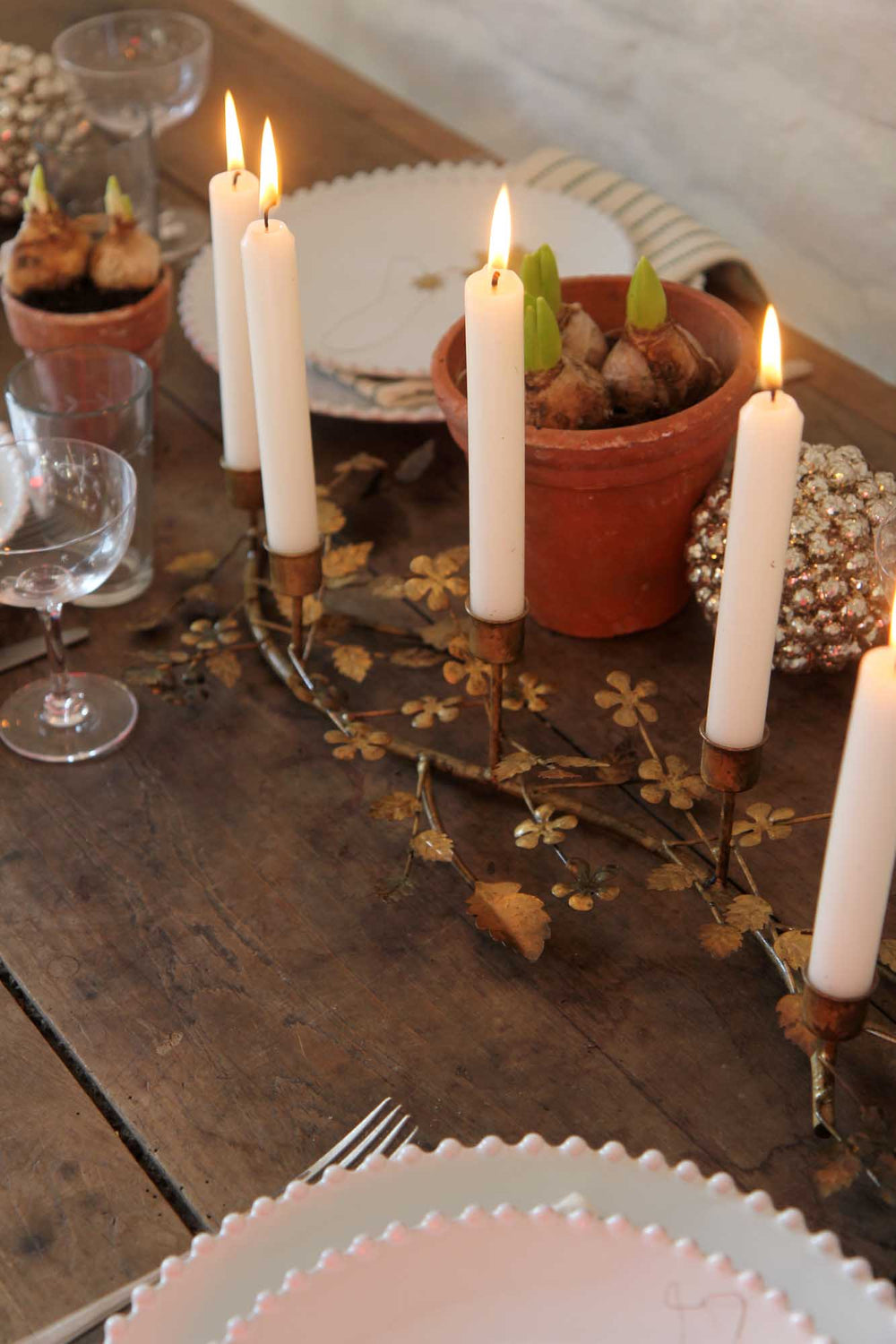 Decorative table setting with candles, potted plants, and cutlery on a wooden surface.