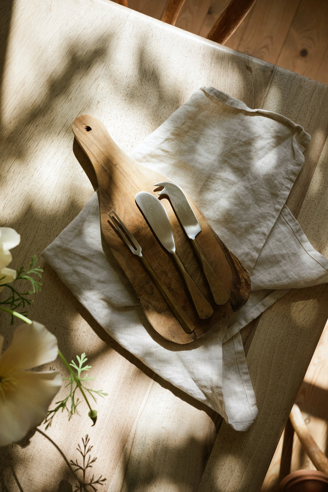 Wooden cutting board with knives on a light fabric surface with flowers in the background