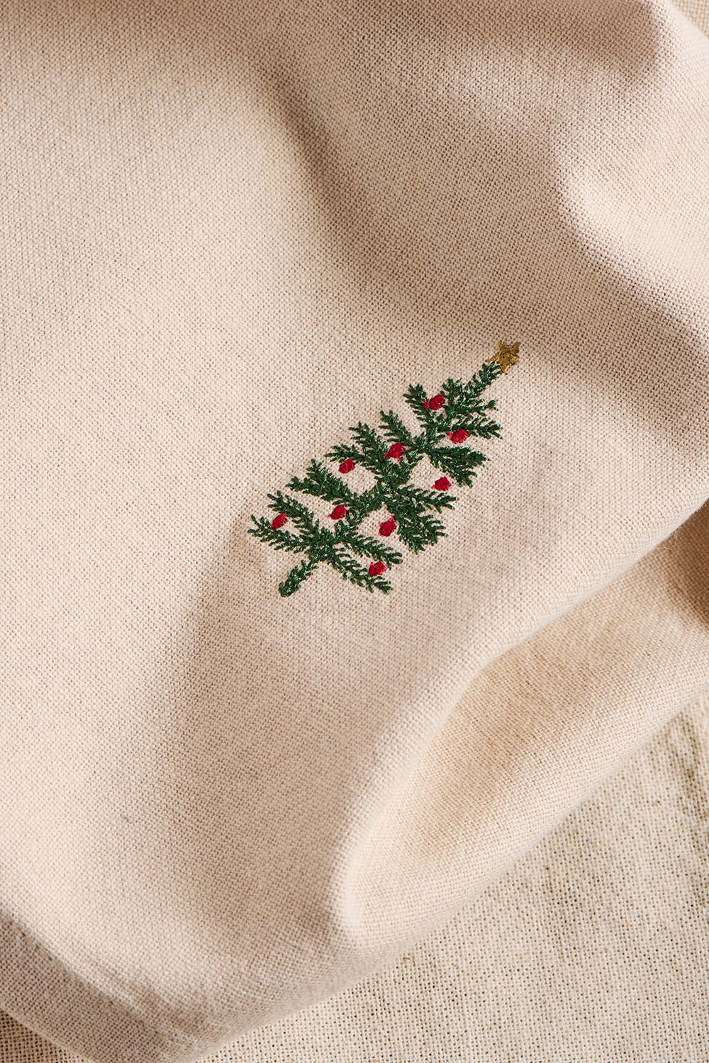 Embroidered Christmas tree design on a beige fabric background