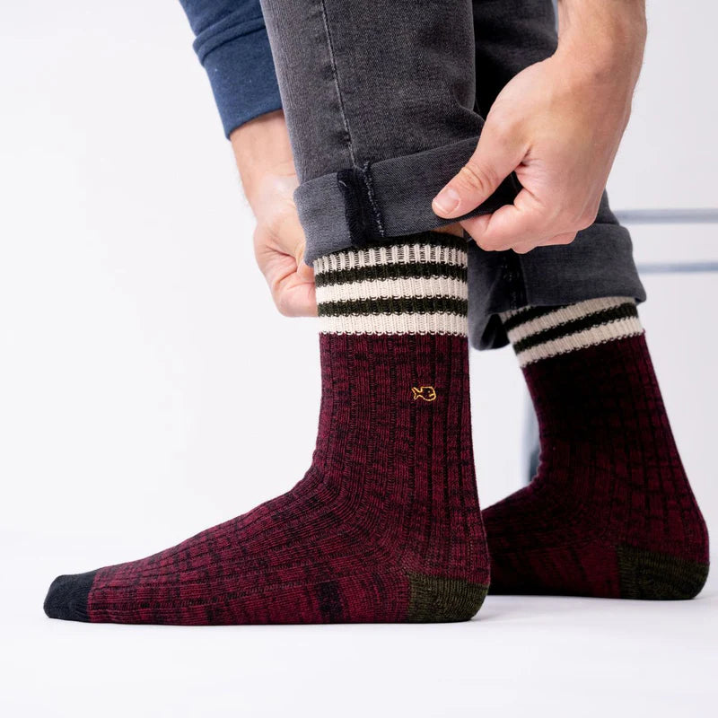 Person wearing maroon socks with white and black stripes, standing on a light gray background