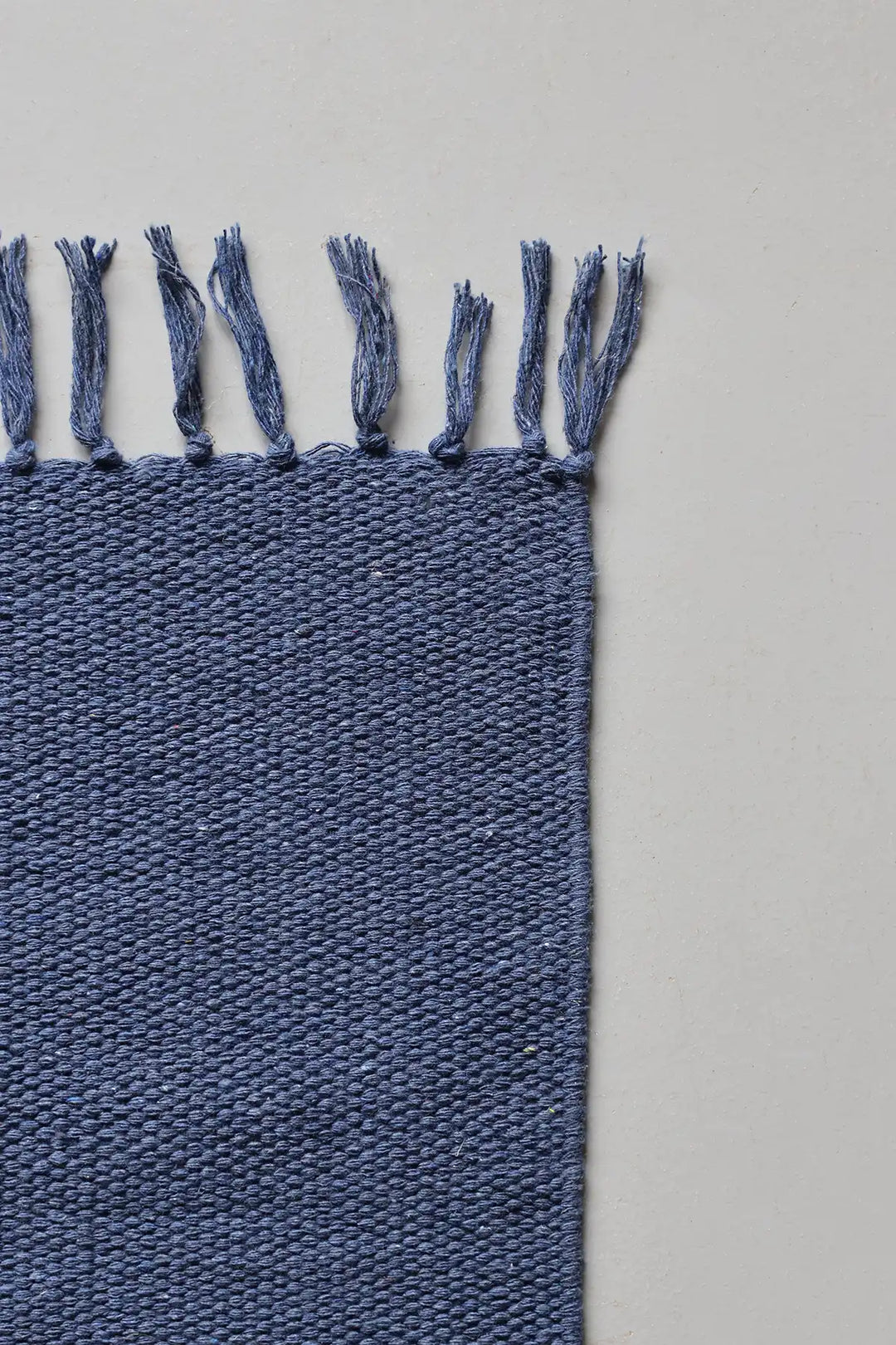 Denim Blue woven rug with tassels on a light gray background