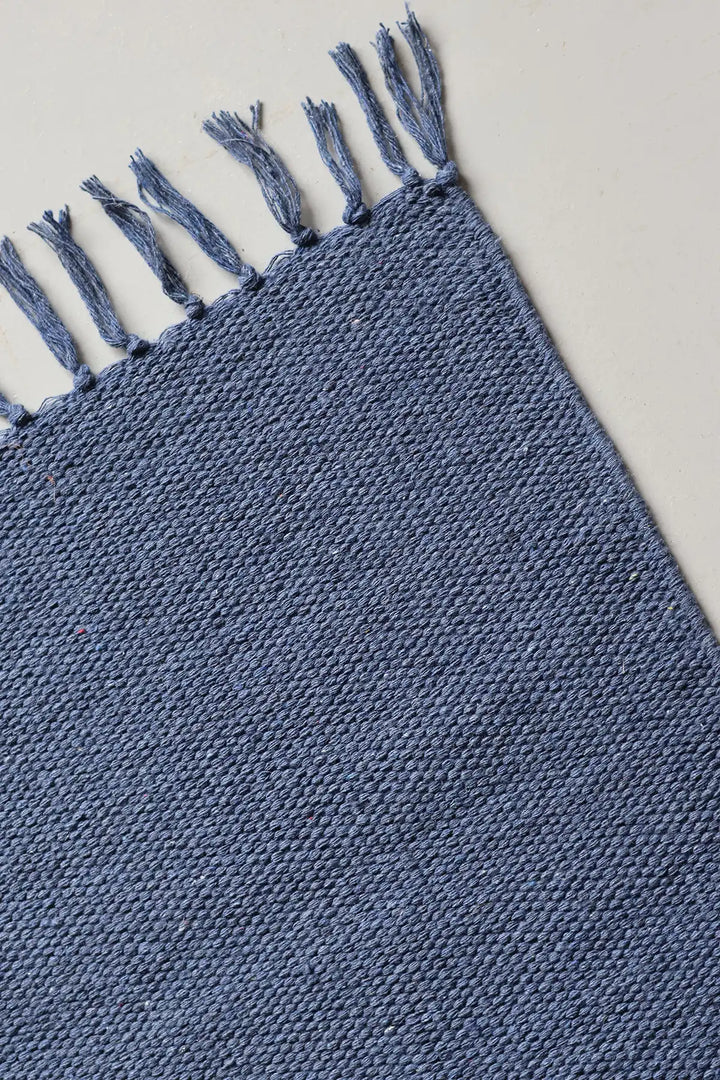 Blue woven rug with tassels on a light gray background