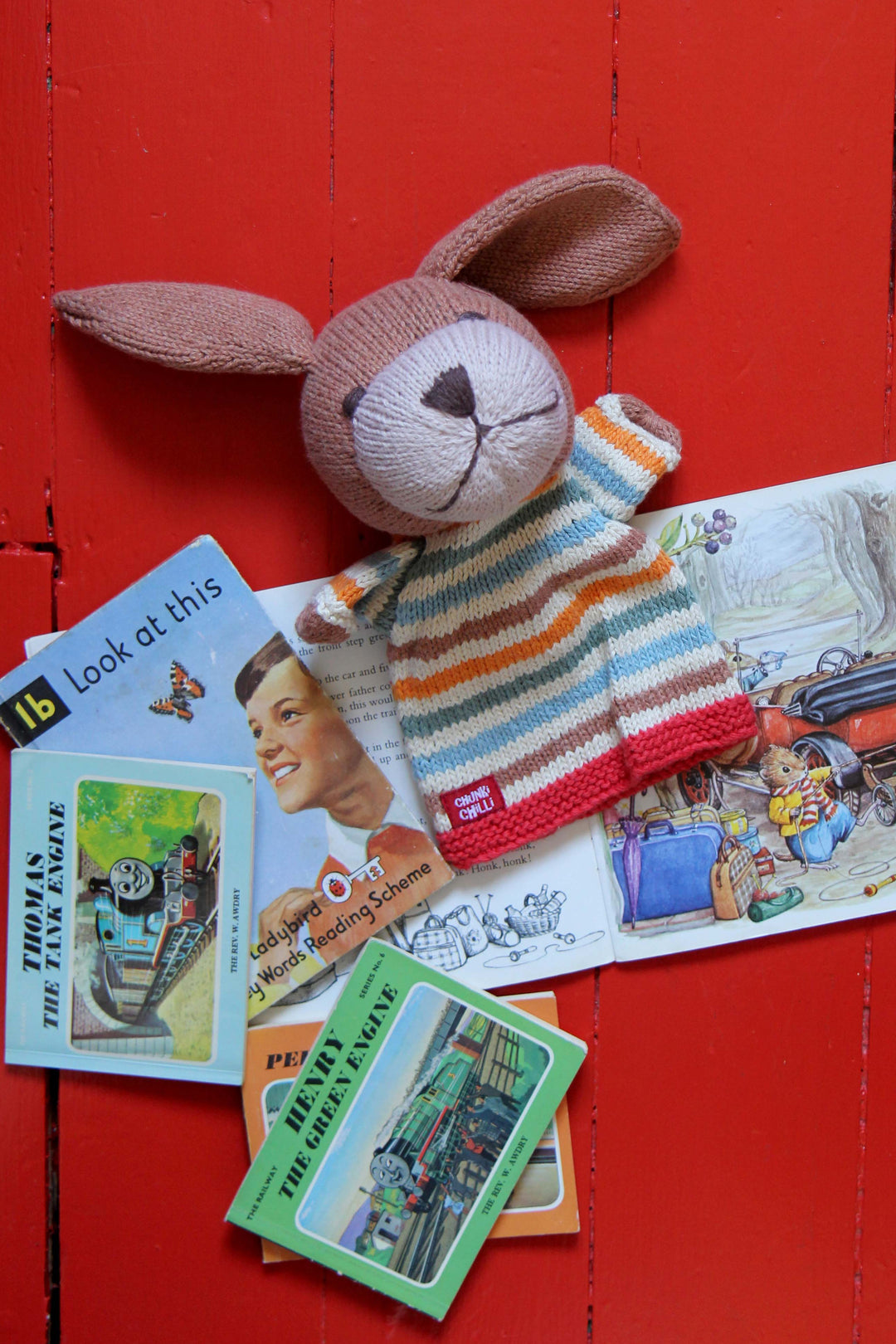 Knitted dog puppet with a striped sweater on a red wooden surface with vintage cards.