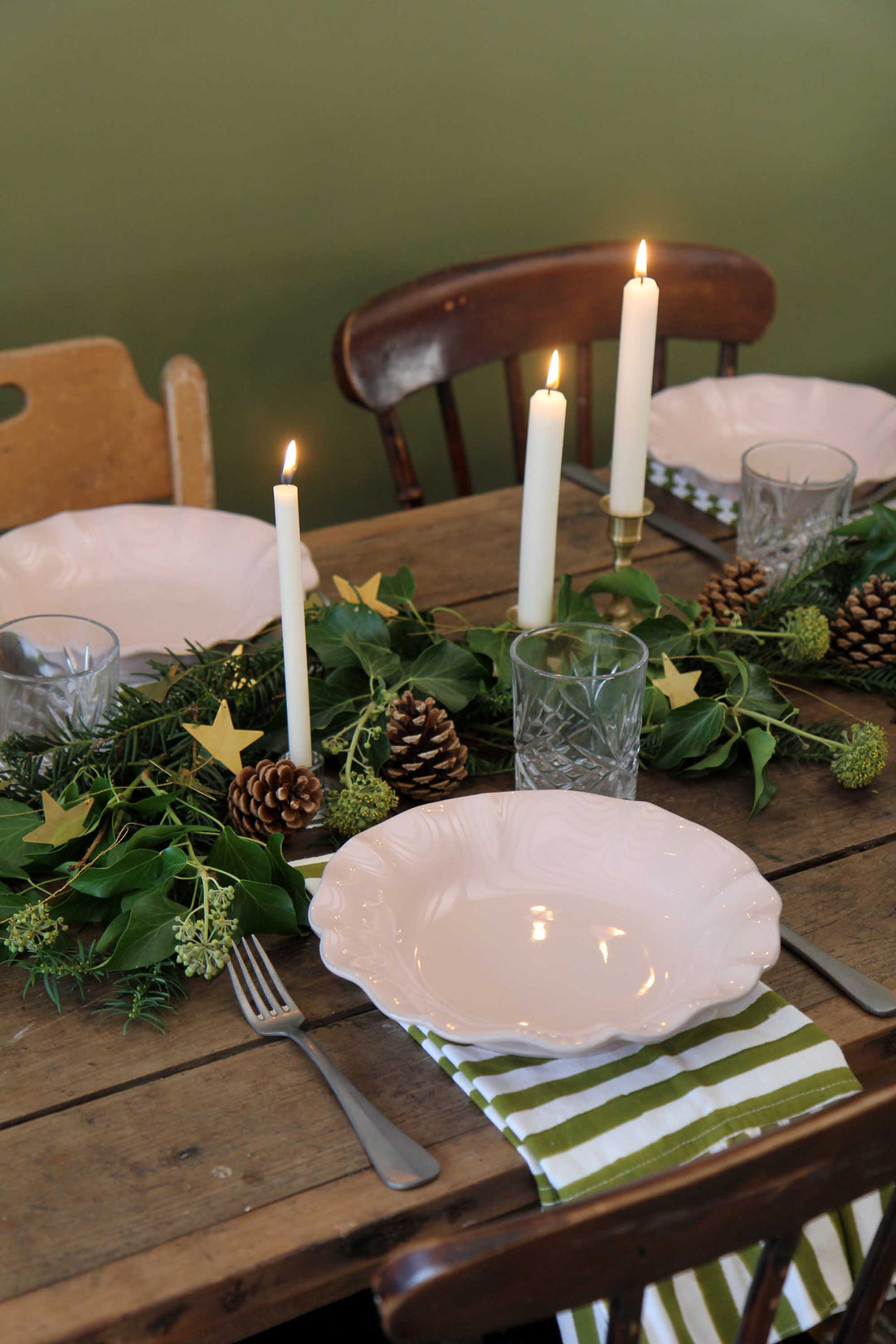 Set christmas dining table with candles, greenery, and a plate on a wooden table.