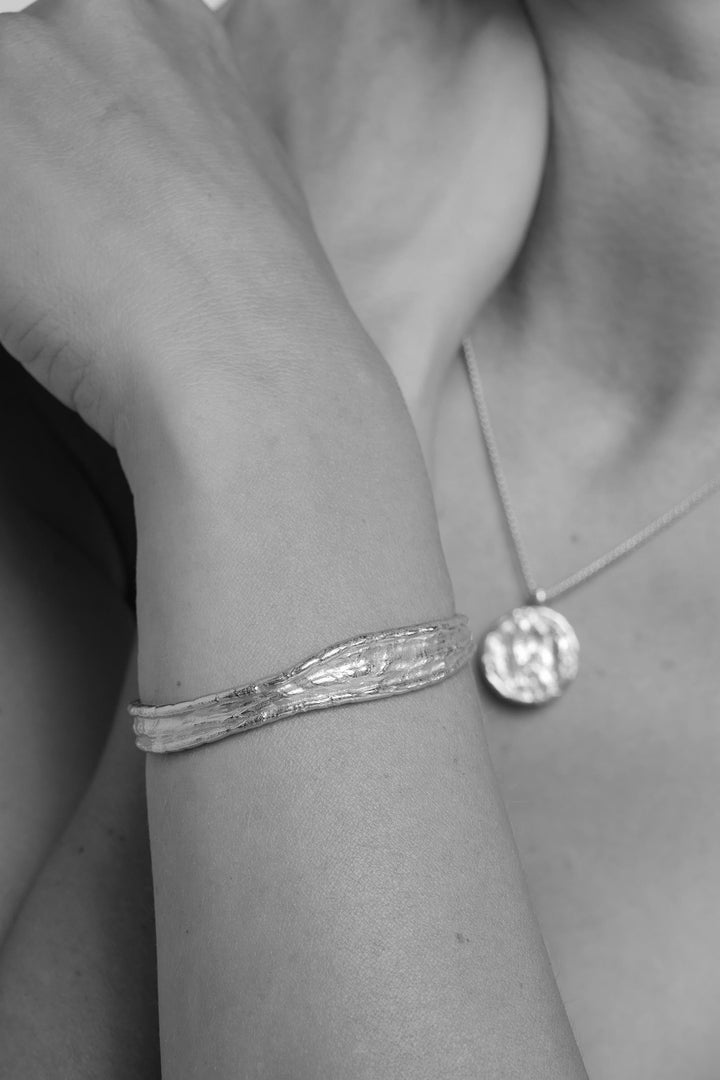 Close-up of a person wearing a silver driftline bangle and necklace.