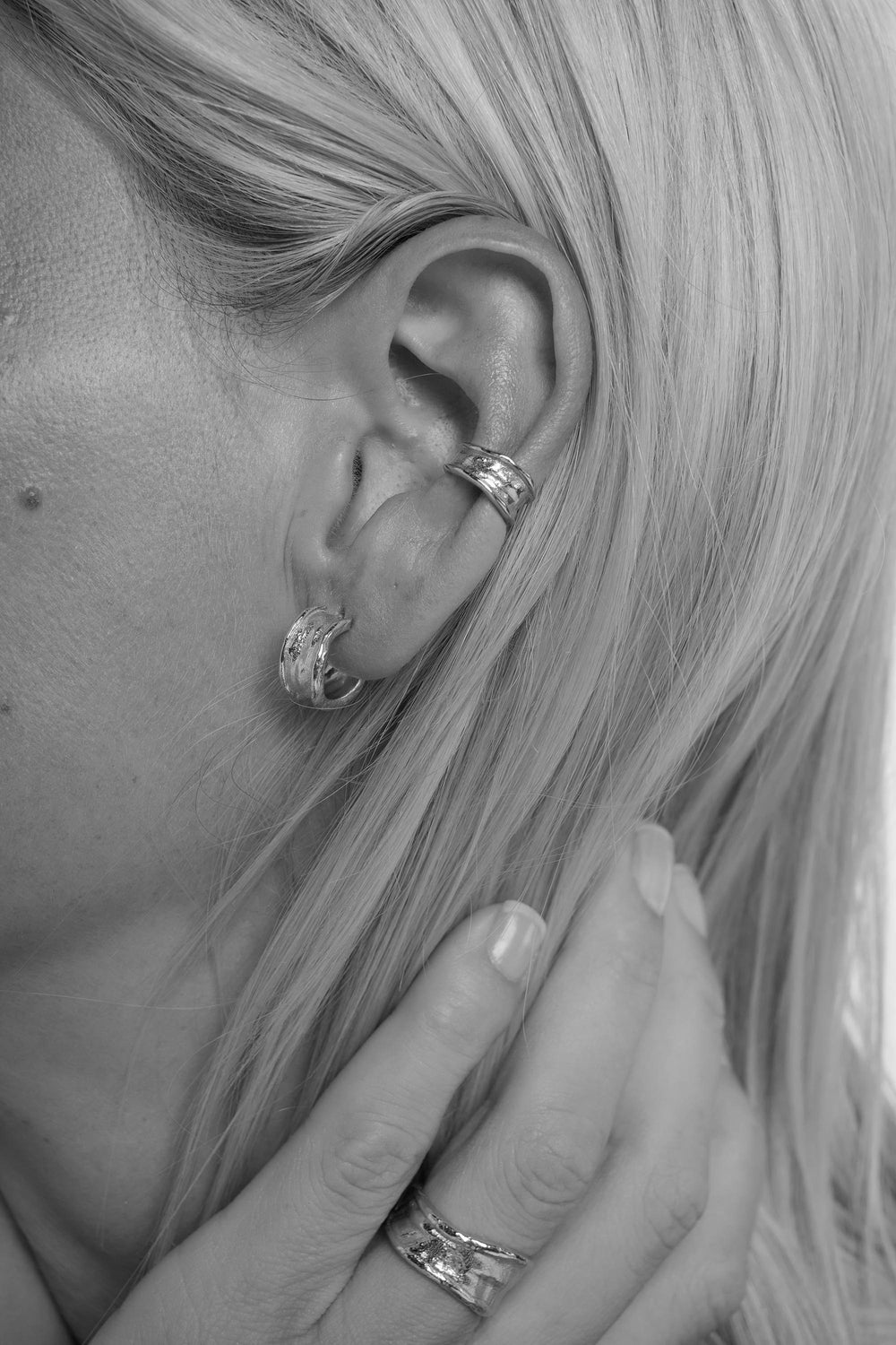 Close-up of an ear with earrings and rings, with hair partially covering the face.
