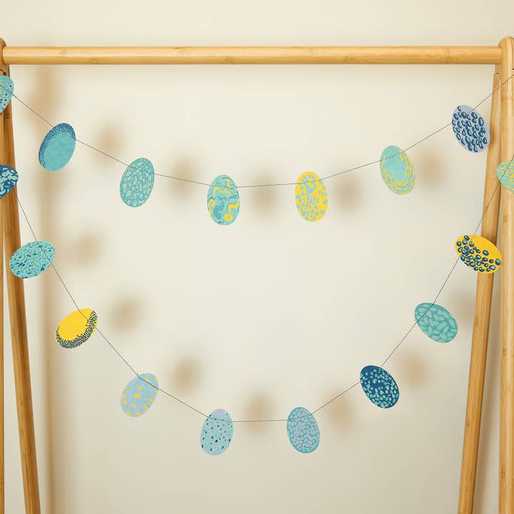 Decorative banner with blue and yellow egg-shaped ornaments on a wooden frame against a beige wall.