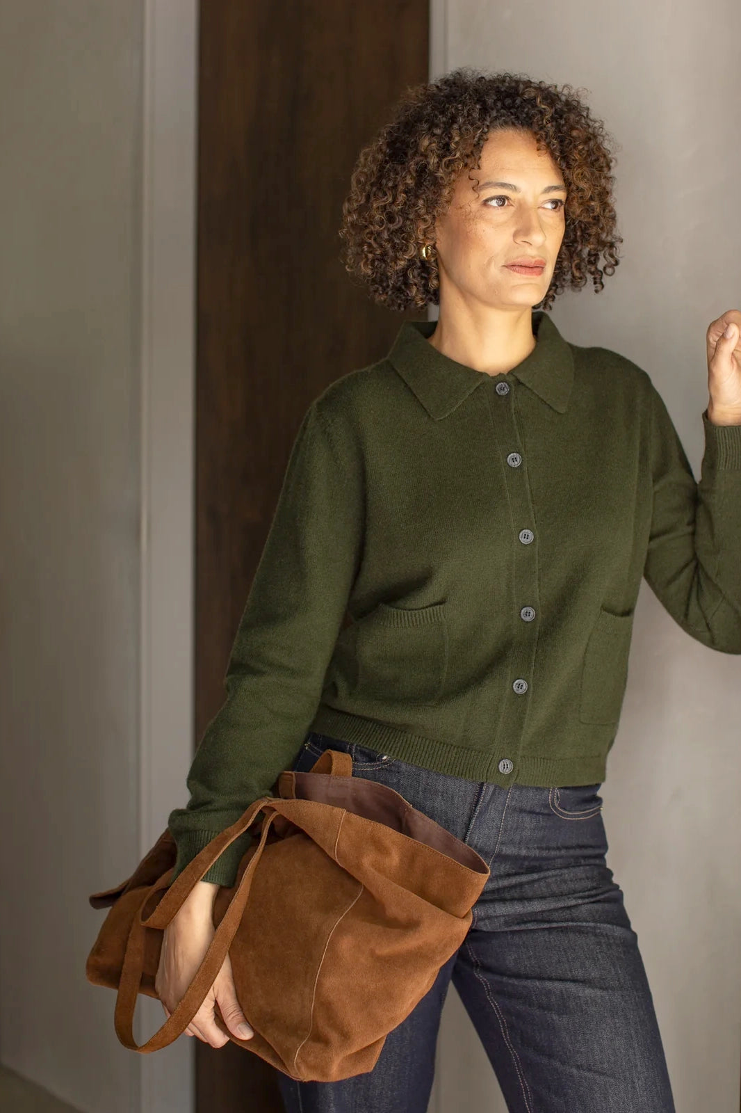 Woman wearing a green cardigan and holding a brown bag against a neutral background