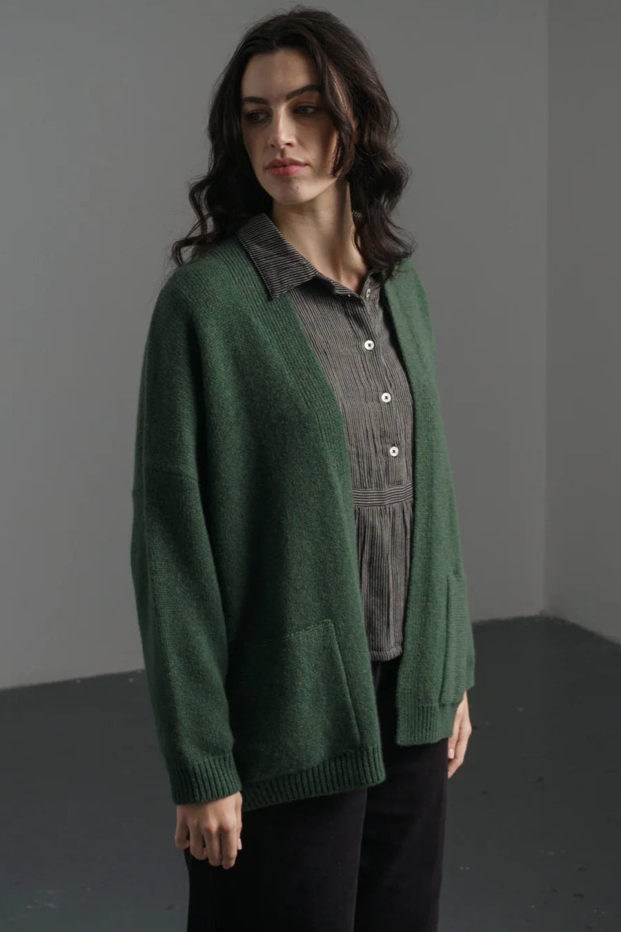 Woman wearing a green cardigan over a gray shirt in a minimalistic setting